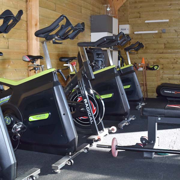 Salle annexe du camp d'entraînement d'Elite Forme équipé de vélos et de matériel de musculation (charriot de charge et haltères).